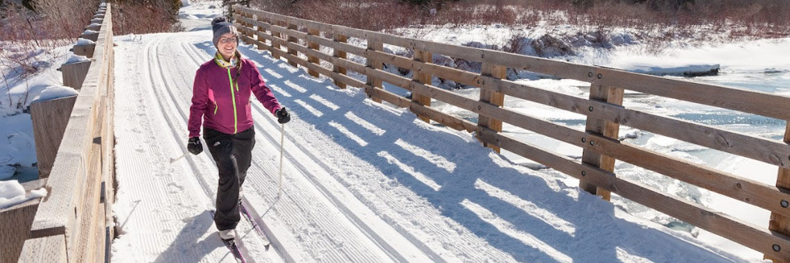 A skier on a bridge over frozen water in Forillon National Park.