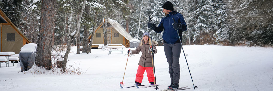 An adult and child cross-country skiing near the oTENTik tents in Riding Mountain National Park.