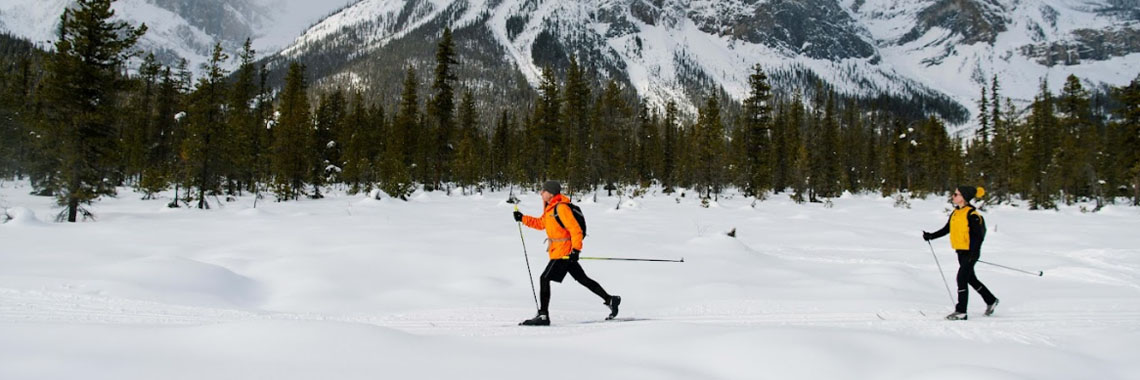 Two people cross-country skiing with mountains in the background at Yoho National Park.