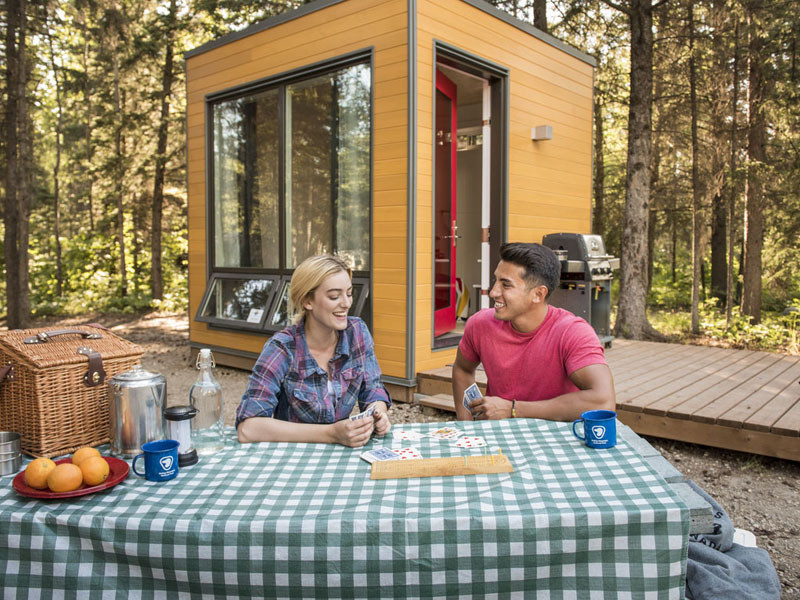 A couple plays cards outside of a MicrOcube accommodation at Wasagaming Campground in  Riding Mountain National Park.