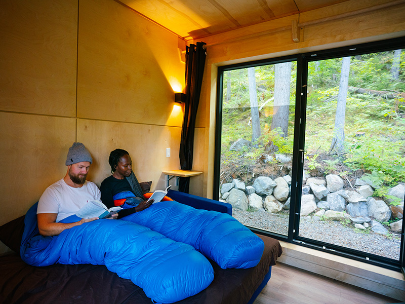 A couple in sleeping bags read books in their MicrOcube accommodation