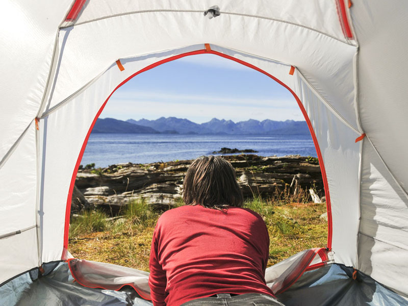 A woman lying down in her tent, looking at the shore in Gwaii Haanas.