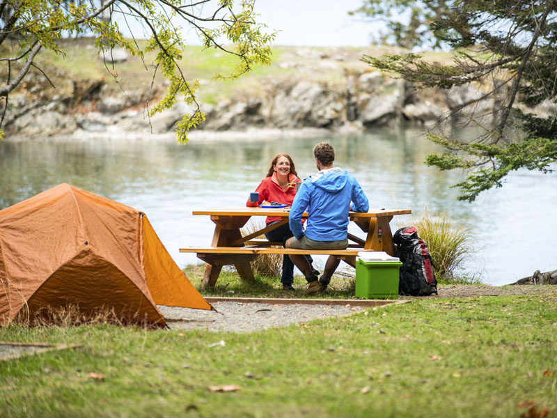 A couple sitting at the picnic table of their waterside campground.