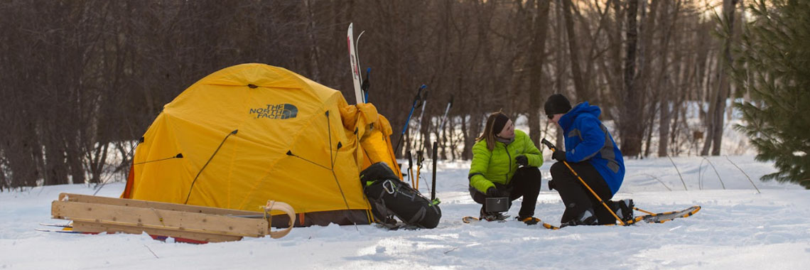 Two people next to their tent in winter at Kouchibouguac National Park.