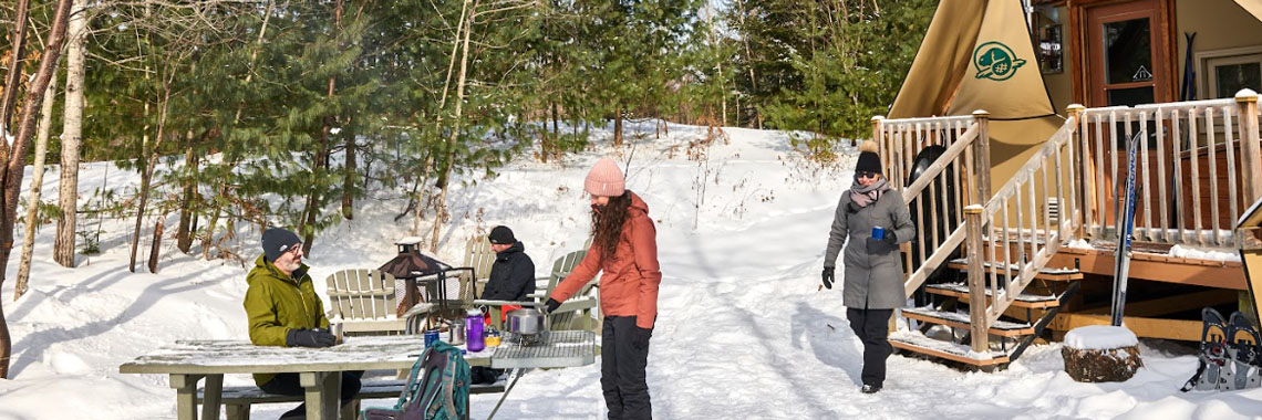 Four people near the outdoor fireplace and table at their oTENTik tent site in La Mauricie National Park.