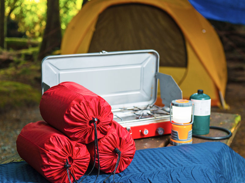 Sacs de couchage, matelas de sol, réchaud de camping, lanterne et tente sur un site de camping.