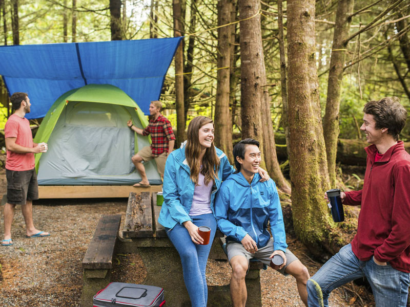 Cinq jeunes adultes discutent près d'une tente et d'une table de pique-nique.