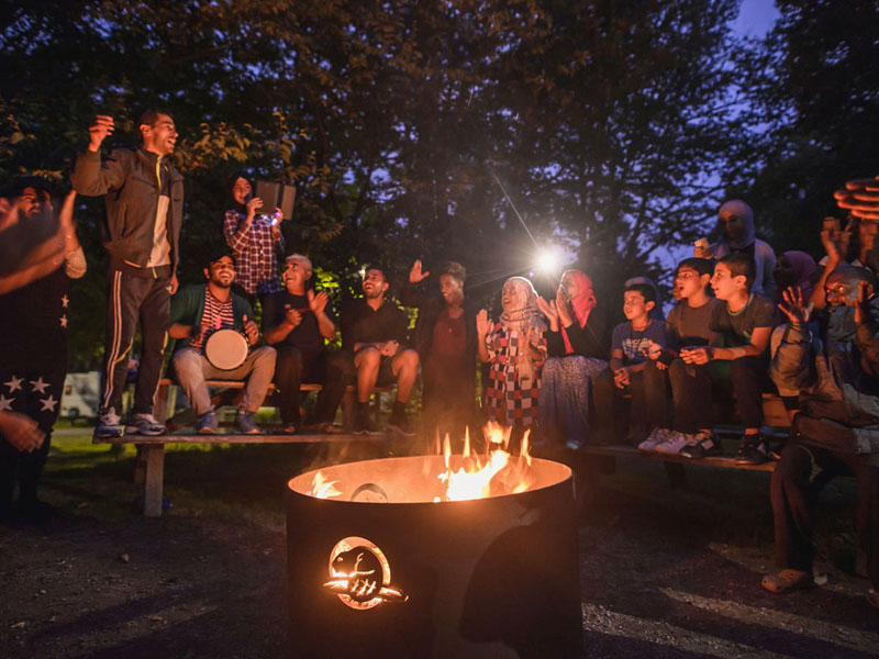 Des néo-Canadiens jouent de la musique et dansent joyeusement autour d’un feu de camp.