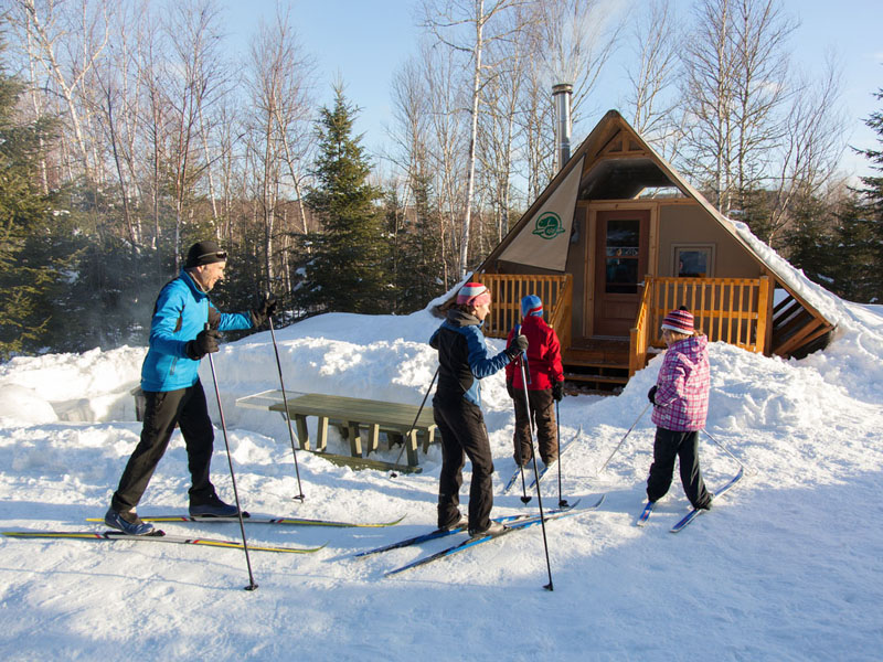 Une petite famille arrive en ski de fond devant leur tente oTENTik.