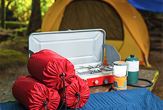 Sleeping bags, a sleeping pad, a camping stove, a lantern and a tent placed at a campsite.