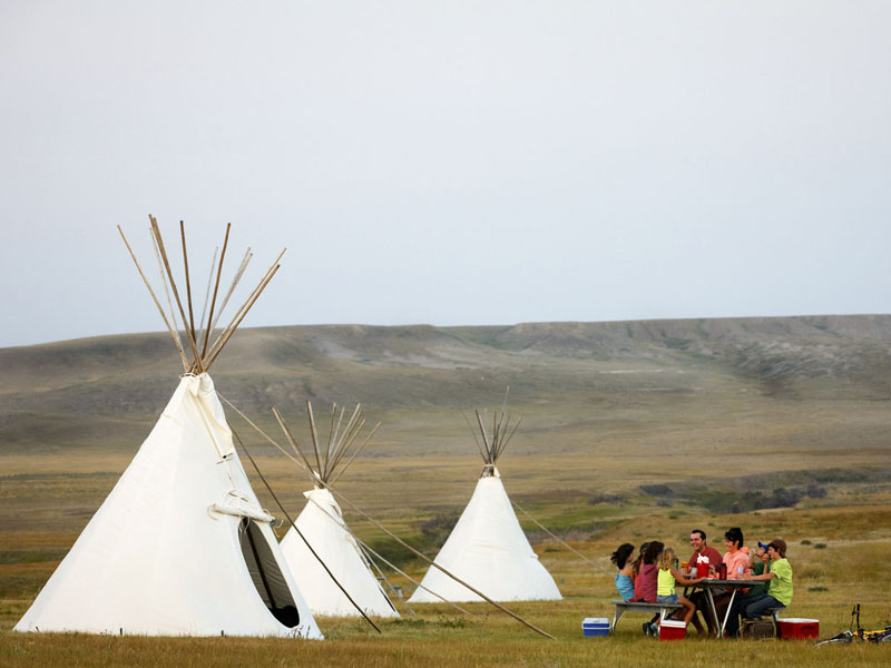 People having a picnic near a tipi. Children playing ball.