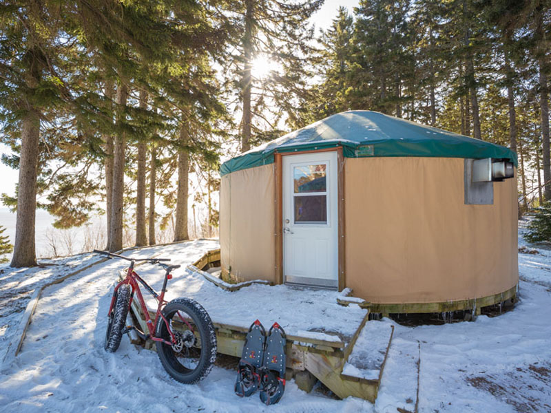 A fatbike and a pair of snowshoes are leaning against the patio of a yurt.