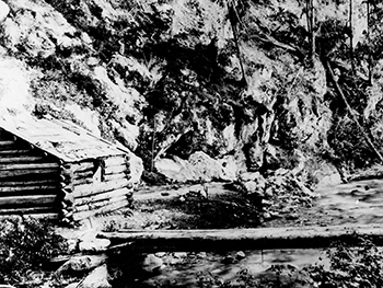 Vestiaire en rondins et pont près du ruisseau Sinclair et des sources thermales Radium. Photo granuleuse en noir et blanc.