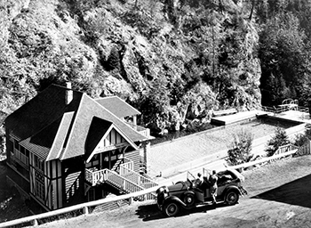 Two people in Ford Motel T admiring the concrete pool and bathhouse from the roadway