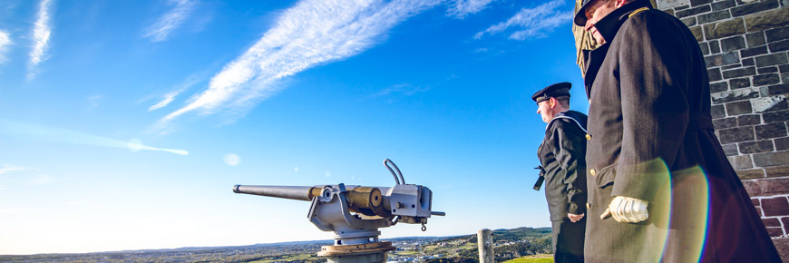 Two men are standing next to the Hotchkiss gun near the Cabot Tower on the hill.