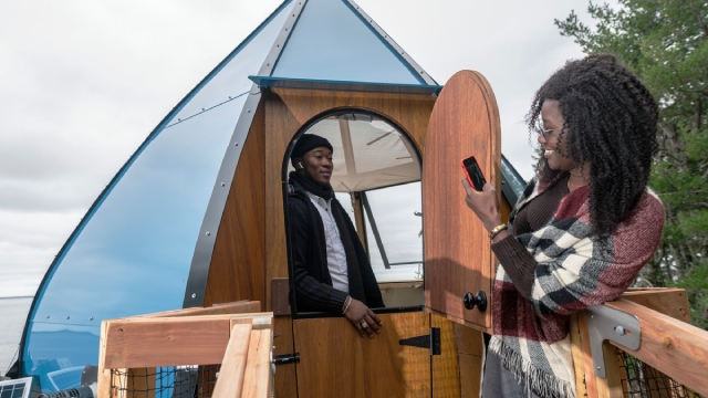 Two adults next to the door of an Ôasis, a teardrop-shaped accommodation.