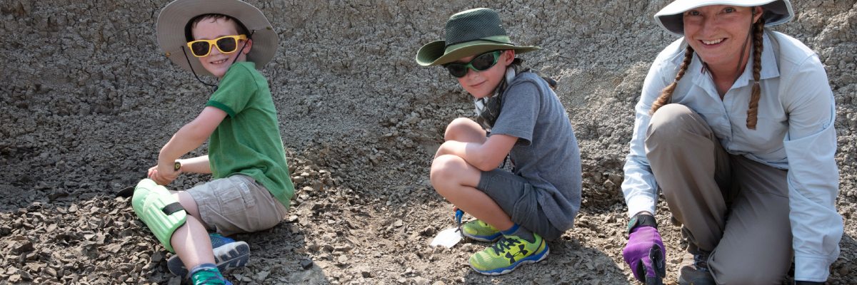 A woman and two children with trowels digging in gravel.