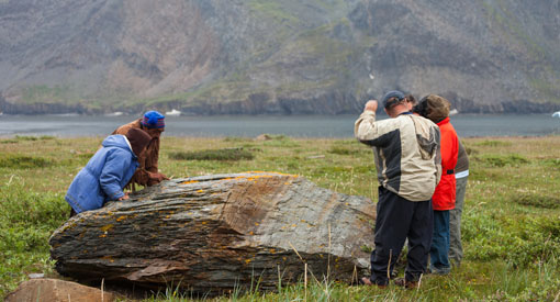 Des visiteurs inspectent une grosse roche en bordure de la rivière.