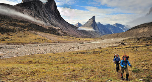A couple walks in the tundra with mountains in the background.