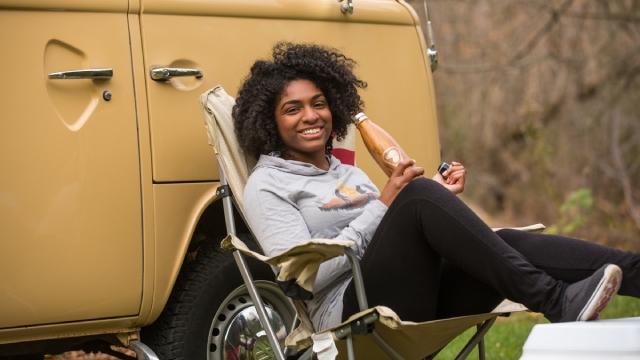 A young woman smiling in her lawn chair in front of her Westfalia.