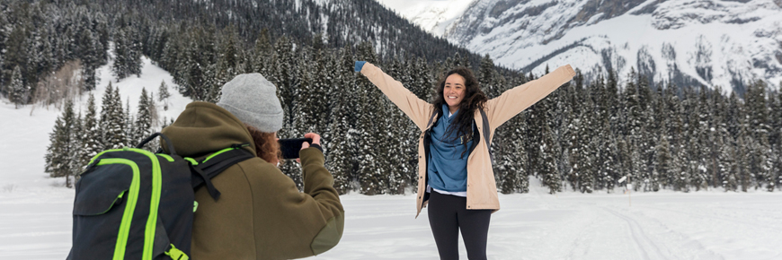 Un jeune homme prend une photo d’une femme dans un paysage hivernal montagneux au parc national Yoho.