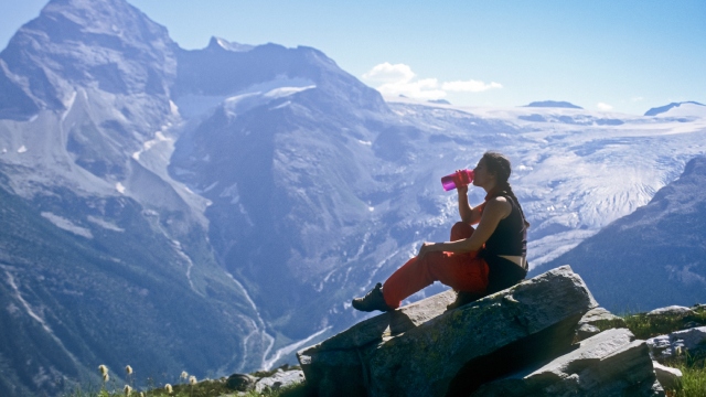 A young woman taking a break from hiking as she sips from her water bottle in front of a mountain panorama.