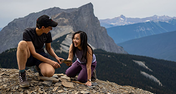 Two visitors look at fossils with mountains in the background in Yoho.