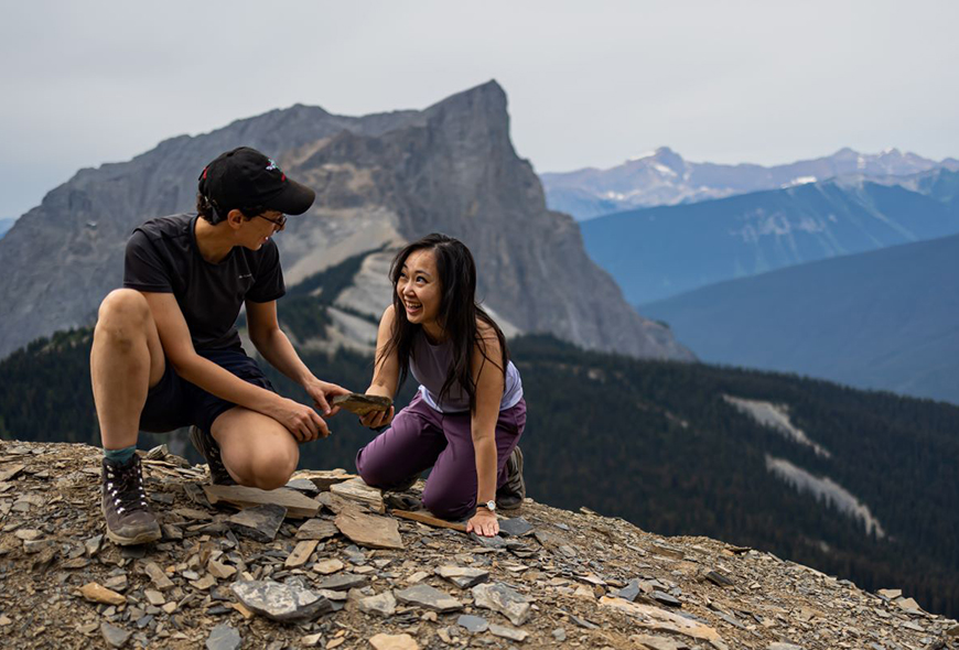 Two visitors look at fossils with mountains in the background in Yoho.