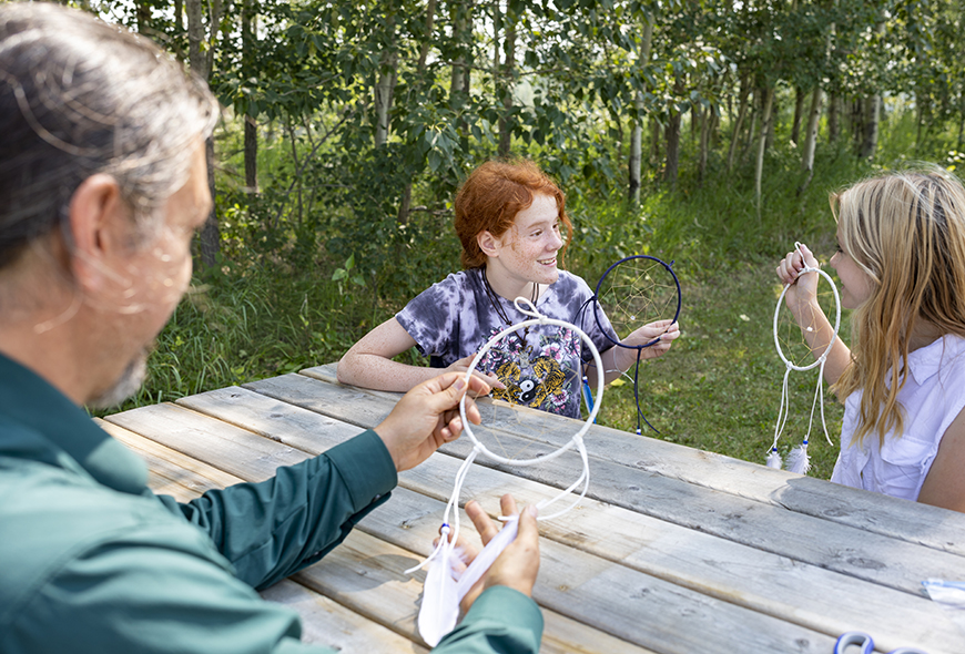 A guide and two young people make Dream Catchers at a picnic table in Rocky Mountain House.