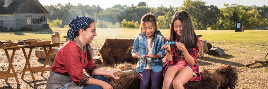 Young visitors learn about beadwork with the help of a costumed animator at the Indigenous encampment.