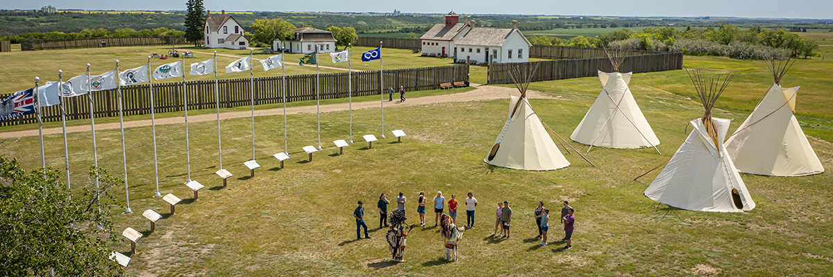 Des visiteurs sur les terrains du fort Battleford avec des tipis et des bâtiments en arrière-plan.