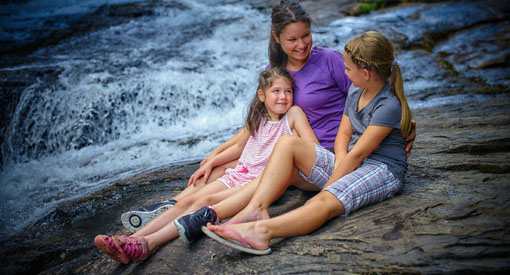 A mother and her two young girls rest next to the waterfalls.