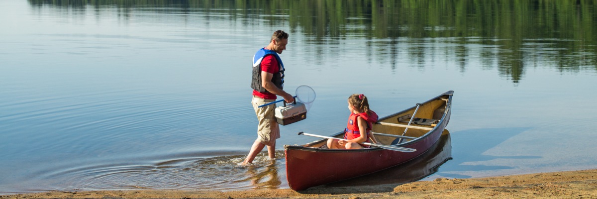 Une jeune fille assise dans un canot, attendant son père apportant le matériel de pêche.