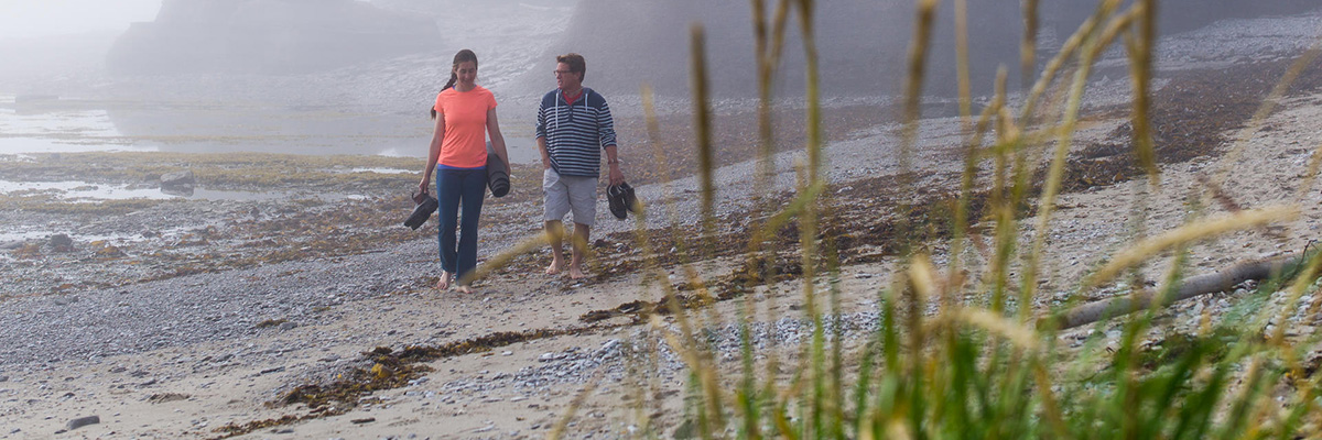 Two visitors walking on a pebble beach with monoliths in the background in the Mingan Archipelago.