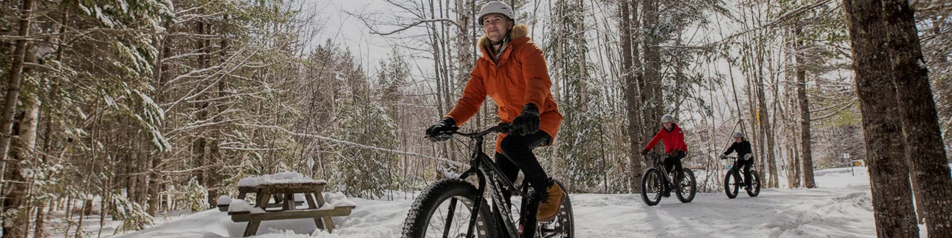 Trois personnes pratiquant le fat bike sur un sentier en hiver.