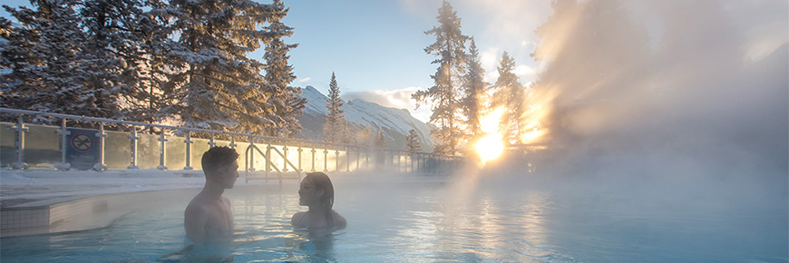 Un couple profite des sources thermales au lever du soleil sur les montagnes, par une matinée froide et enneigée. 