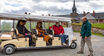 Un groupe de personnes dans une voiturette de golf écoute leur guide lors d'une visite guidée motorisée à la forteresse de Louisbourg.