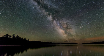 Une famille regarde une réserve de ciel étoilé à l'aide d'un télescope à côté d'un guide de Parcs Canada au cercle céleste au parc national et lieu historique national Kejimkujik.