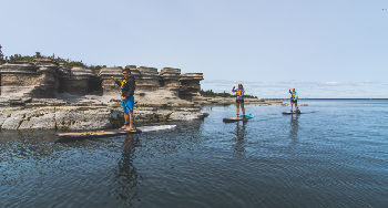 Three people are doing a SUP excursion close to the cliffs of an island.