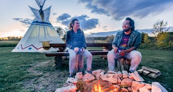 2 amis qui parlent à côter d'un feu et en avant d'un tipi