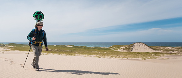 A Parks Canada team member walking with a Google Trekker, a 360o camera.