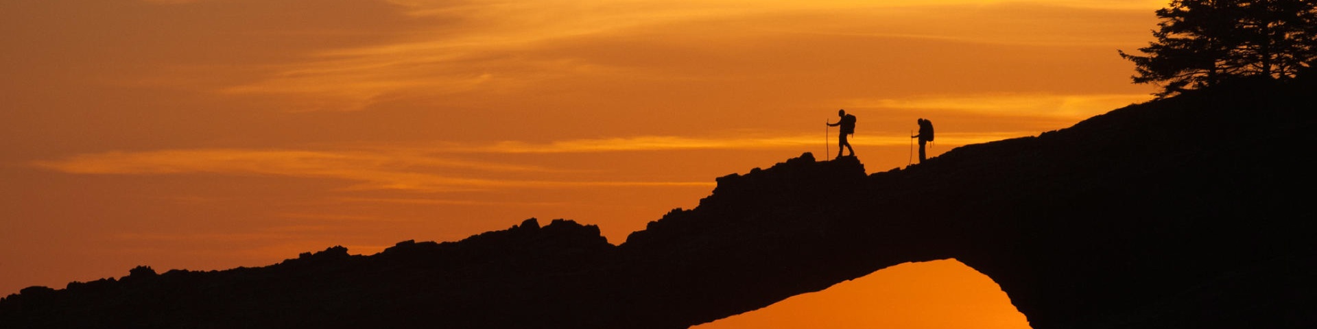 Two people hike along a coastal arch at sunset along the West Coast Trail, Pacific Rim National Park Reserve.