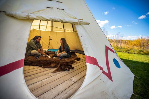 Two visitors are seen playing cards inside a tipi, taken from outside the tipi looking in.