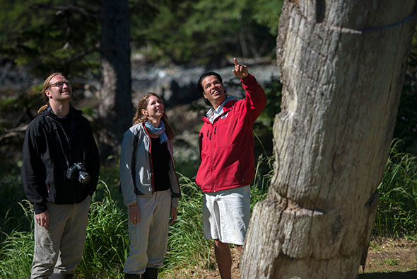 Three adults stand as a Haida Gwaii Watchmen points to remnants of a village site