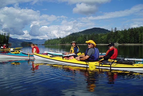 A group of kayakers come together on a calm waterway on a sunny day