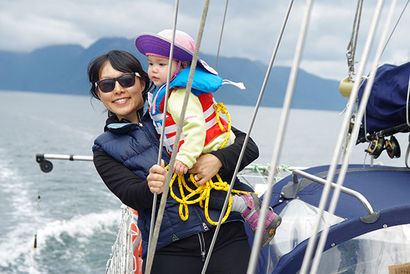 A smiling woman holding a child stands on a sailboat