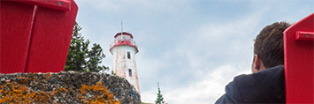 A person sitting in a red chair, looking at a lighthouse.
