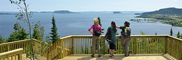Three people standing on a platform overlooking Lake Superior.