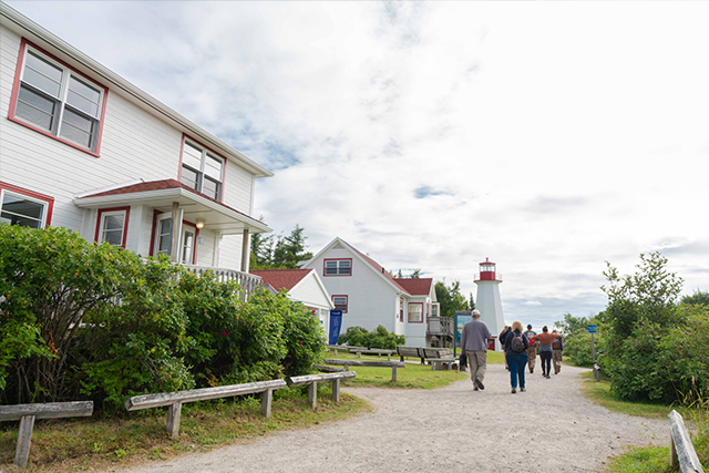 Des gens se promènent entre les différents bâtiments de la station de phare du cap de Bon-Désir.
