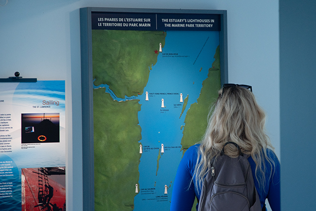 Une dame consulte un tableau des phares de l'estuaire du Saint-Laurent.